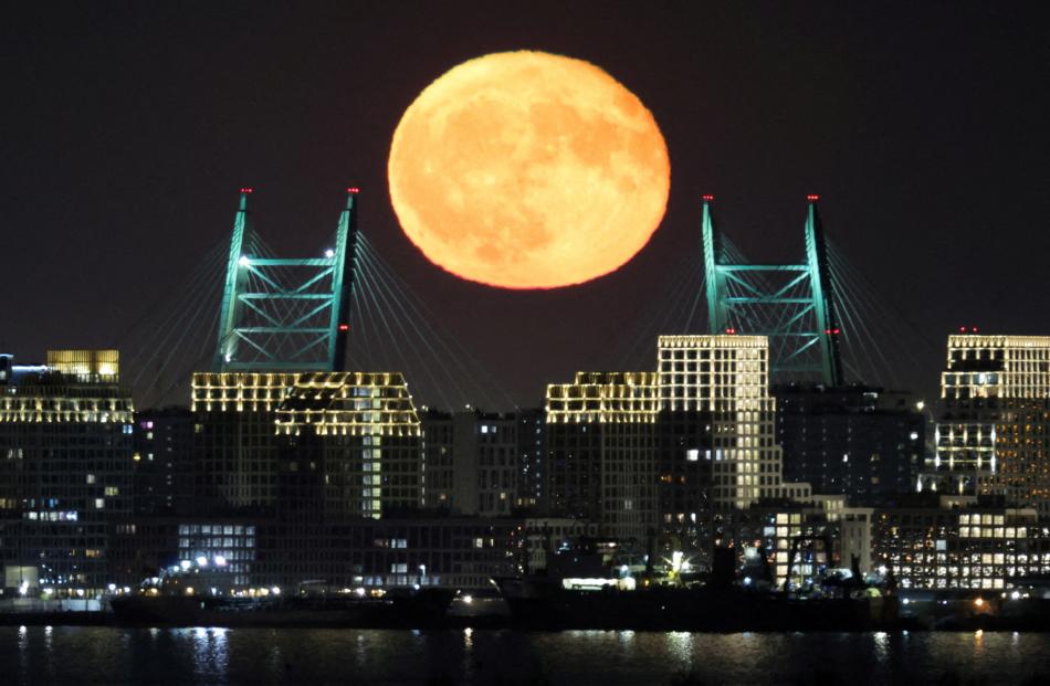 The full moon rises behind a bridge of the Western High-Speed Diameter highway in Saint...