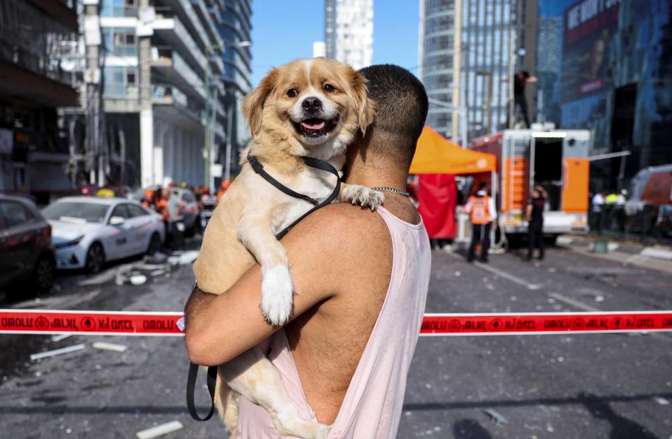 A man carries his dog as he stands at an impact site following a strike from Iran on Israel, in...