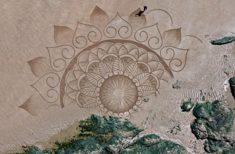 A drone view shows French artist Pierre-Louis Cullier drawing a mandala with a rake on the sand...