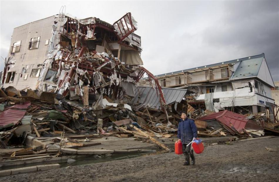 A Japanese man (above) carries water past the remains of damaged buildings after the earthquake...