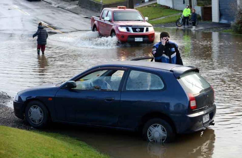 Grant Moore talks on the phone yesterday near a car swept away by flood water in North Taieri Rd,...