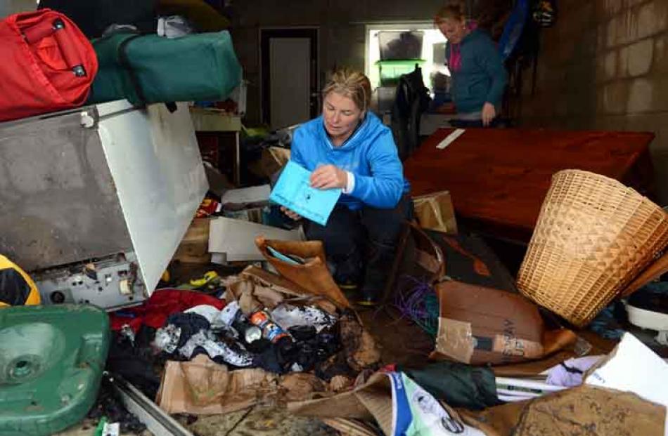 Anna Bartlett (left) inspects the water damaged school reports and photos yesterday in her garage...