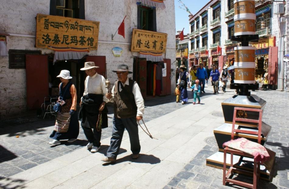 Tibetans, with prayer wheel and beads, walk around the Jokhang Temple pilgrimage circuit. In the...