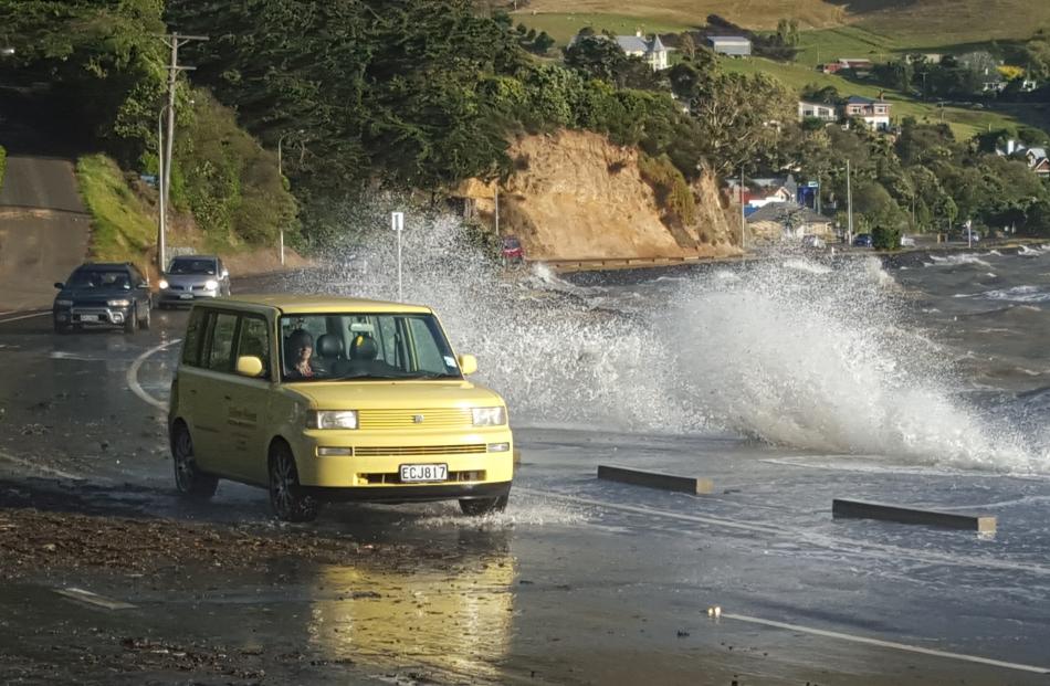 Waves crash over the road at Macandrew Bay. Photo by David Loughrey