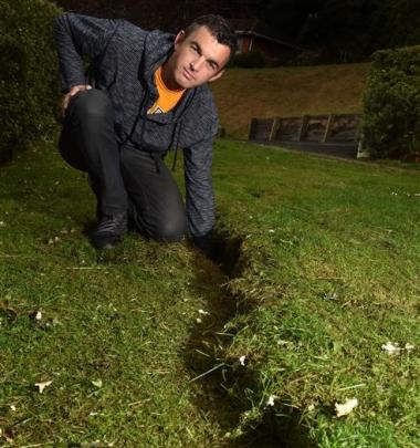 Careys Bay resident Hayden Smith demonstrates the depth of a crack which opened in his front yard...