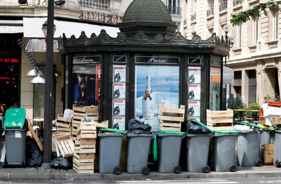 Garbage containers and rubbish bags are seen around a Parisian kiosk selling newspapers and...