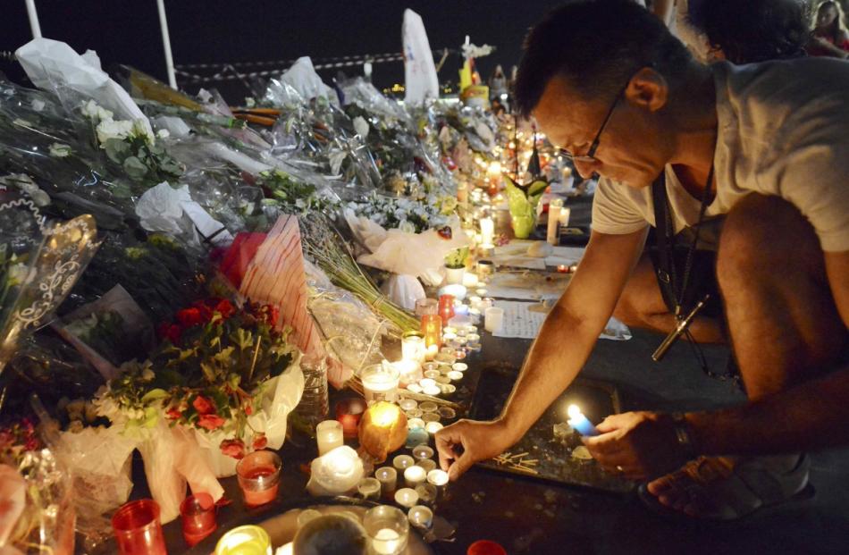 A man places candles near flowers that were left in tribute at makeshift memorials to the victims...