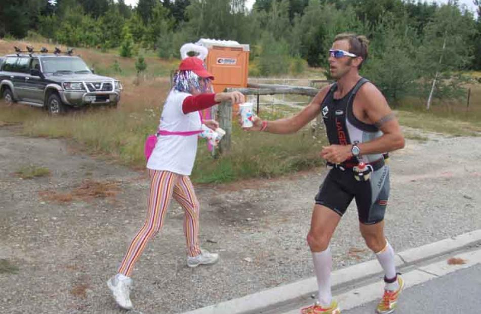 Chris McDonald takes water from Susan Davidson at an aid station on Aubrey Rd, about 15km into...