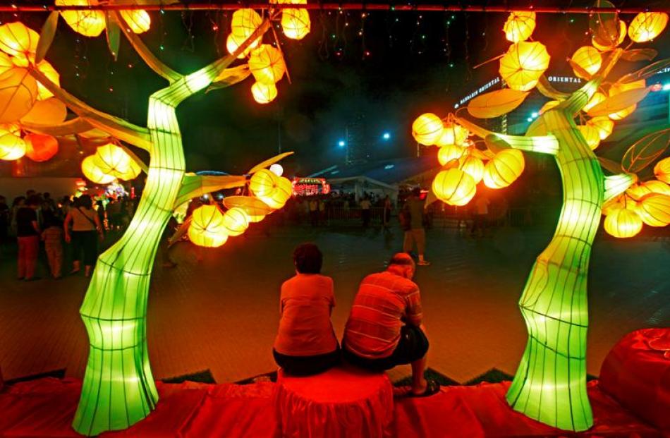 An elderly couple sits under lantern sculptures of mandarin orange trees as they gather to usher...