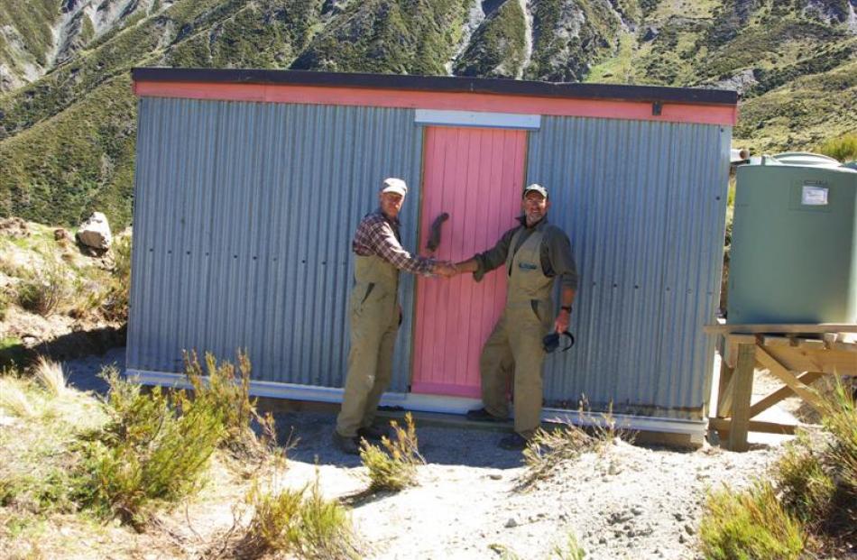 Mr Murfin (left) and Mr Hardie shake hands in front of the restored hut. Photo by DoC.