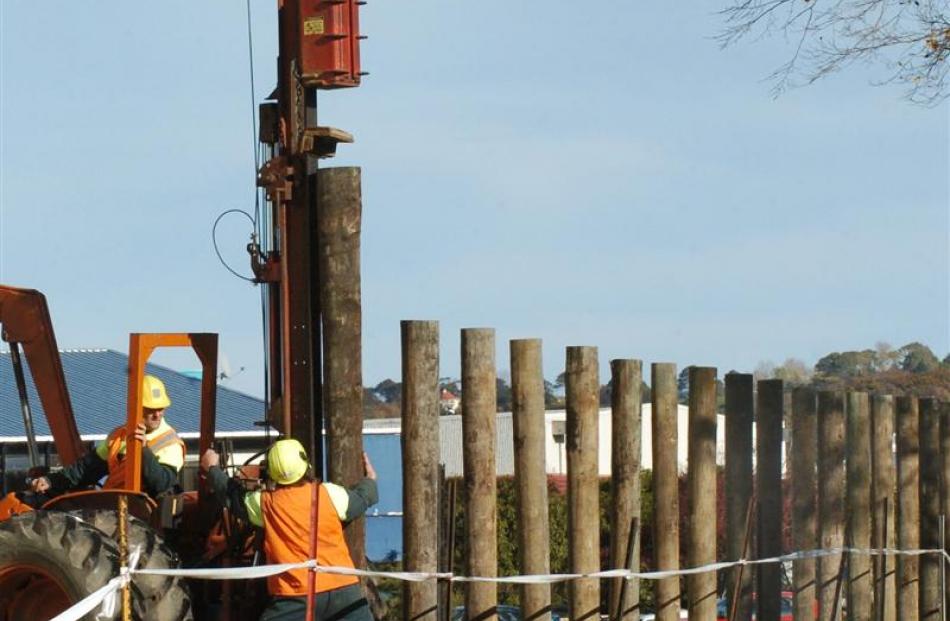 Hawkins Construction workers (top) use a pile-driver to install a security fence around the...