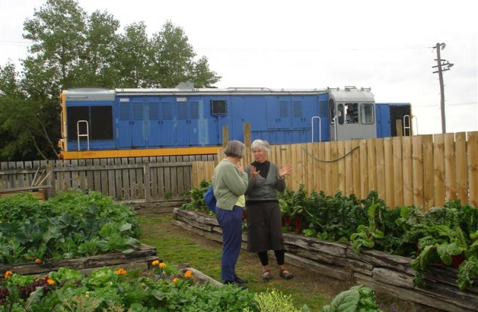 Patricia Bosshard Browne (right) takes a visitor around the garden as a train passes behind.