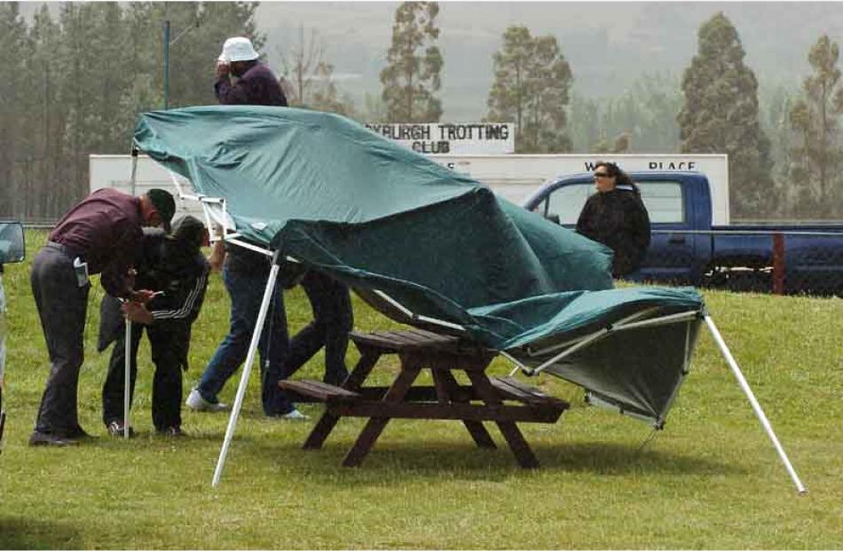 Race- goers struggle to re-erect a gazebo in the wind at the Roxburgh Trotting Club's meeting.