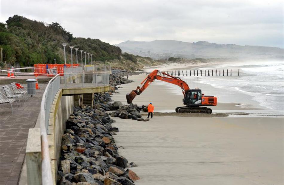 A digger (top) works to clear rocks from the bottom of the St Clair sea wall yesterday in search...