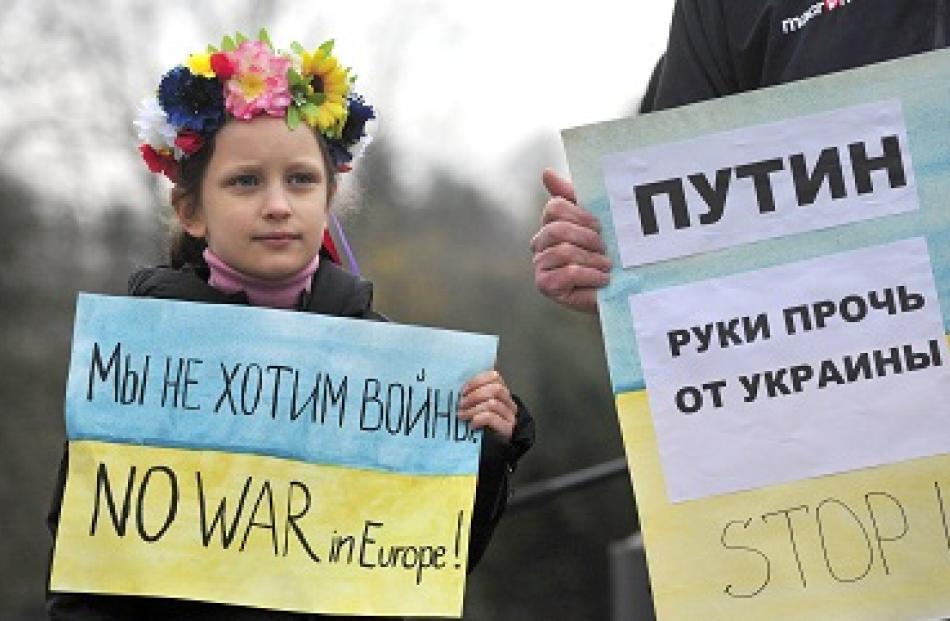 A girl and her father, both members of Slovenia's Ukrainian community, hold signs as they protest...