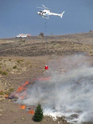 A helicopter crew douses flames on the Bannockburn side of Cornish Point yesterday.