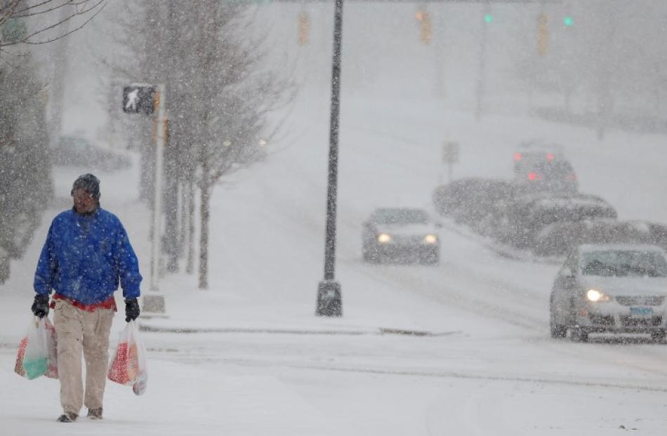 A man carrying groceries makes his way to a bus stop as snow falls in Charlotte, North Carolina....