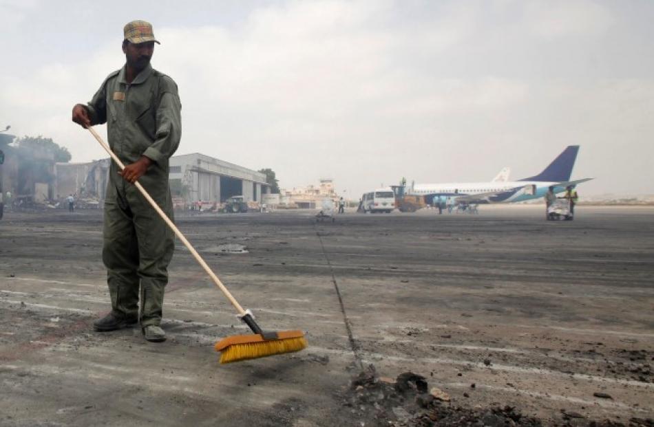 A man clears debris from the tarmac of Jinnah International Airport, after the attack by Taliban...