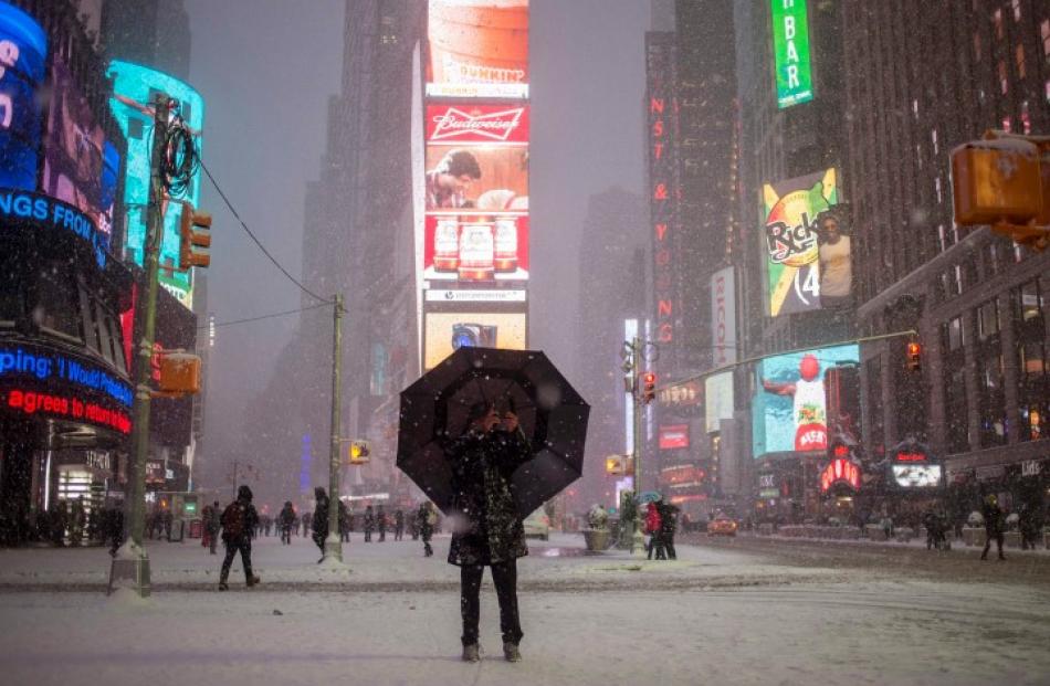 A man stands under an umbrella while photographing a snow storm in Times Square, New York....