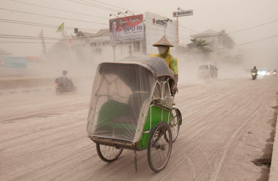 A man wears a mask as he rides a becak, a kind of rickshaw, on a road covered with ash from Mount...