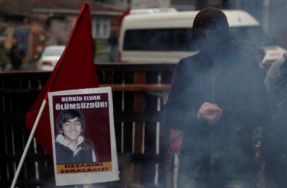 A masked man stands next to a posters with Berkin Elvan's illustration and a slogan reading ...