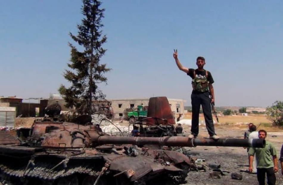 A member of the Free Syrian Army stands on a damaged tank in Jerjenaz, near Idlib. REUTERS/Shaam...