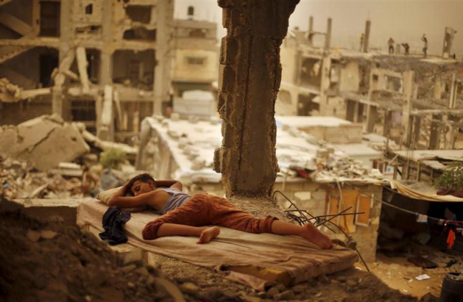 A Palestinian boy sleeps on a mattress inside the remains of his family's house, destroyed by...