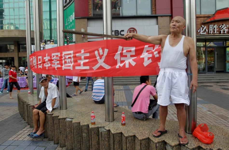 A protester yells anti-Japan slogans as he holds a stick in front of a banner on a commercial...