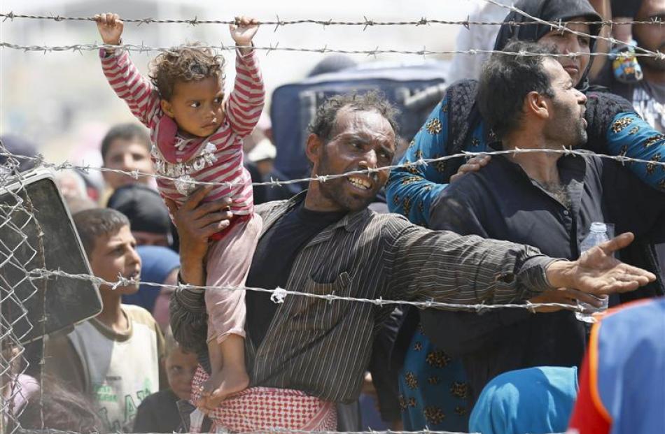 A Syrian refugee holds on to his daughter as he waits to cross into Turkey this week. Photo by...