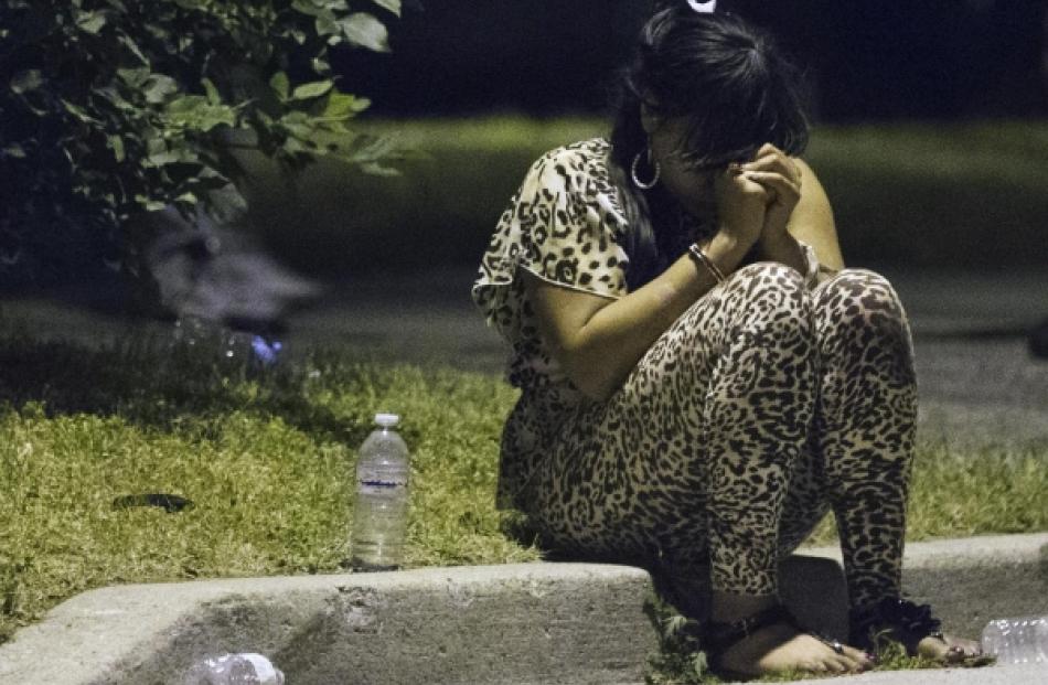 A woman sits on the curb wearing handcuffs at a crime scene following a shooting in Scarborough,...
