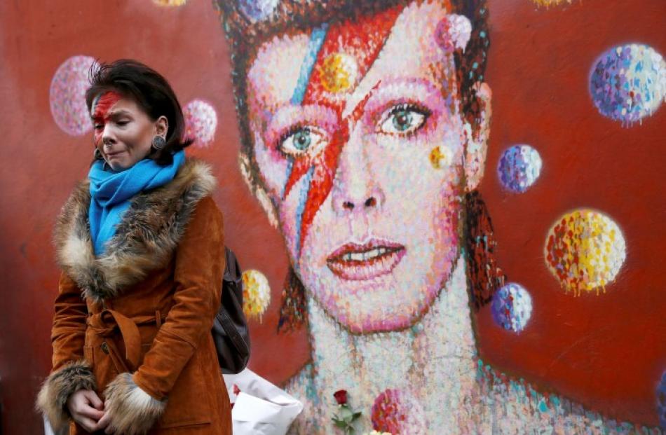 A woman wearing Ziggy Stardust-style make-up mourns by a mural of David Bowie in Brixton, south...