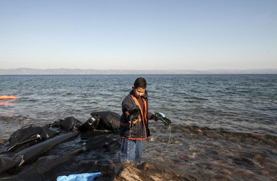 A young migrant empties the sea water from his shoes moments after arriving on a overcrowded...