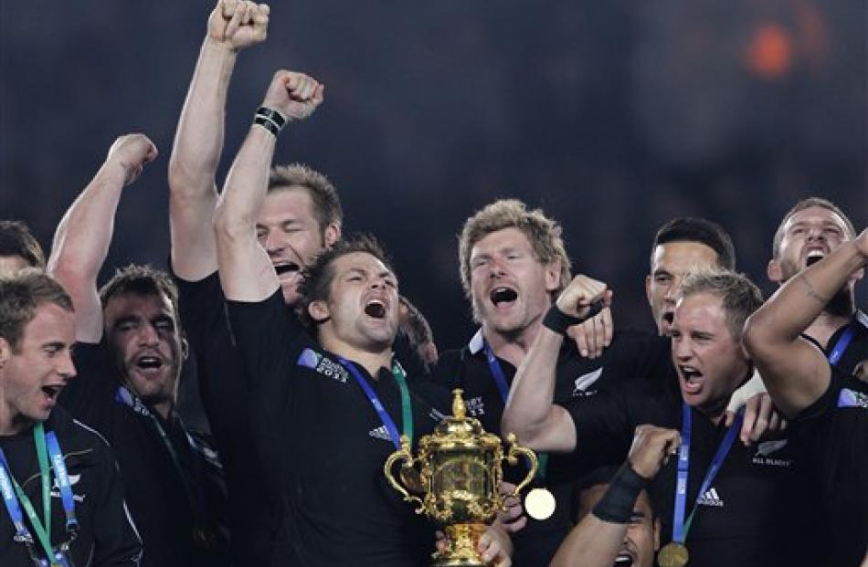 All Black captain Richie McCaw holds the Webb Ellis trophy as teammates celebrate their Rugby...
