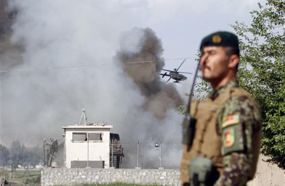 An Afghan soldier stands guard as a helicopter flies low over the scene of a suicide attack on...