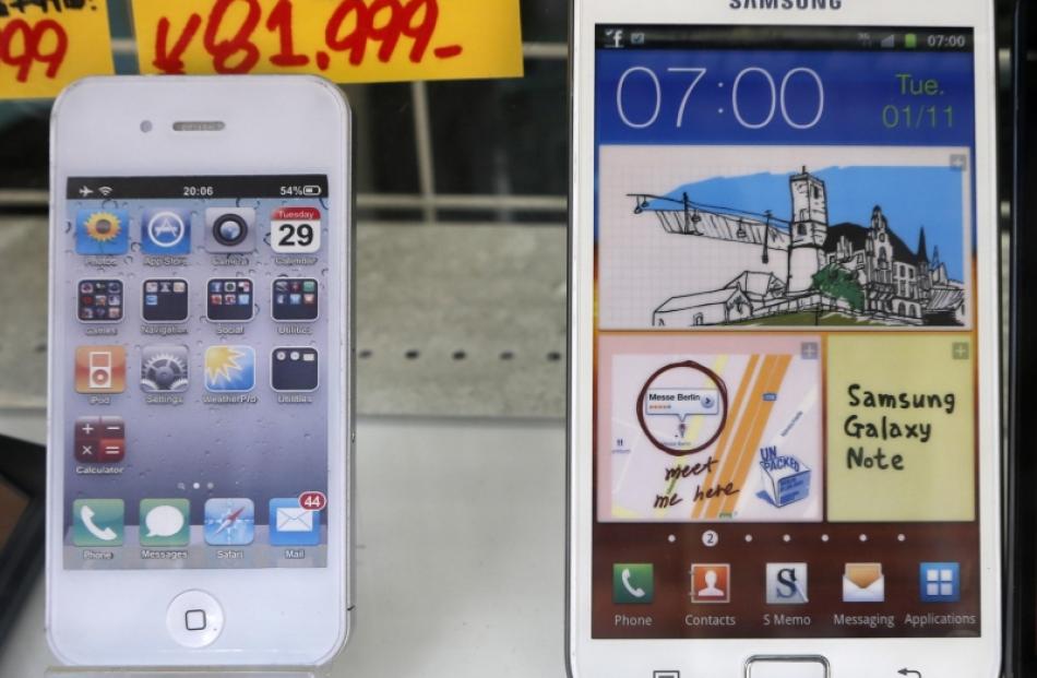 An Apple iPhone (left) and a Samsung Galaxy Note are displayed at a shop in Tokyo. File photo by...