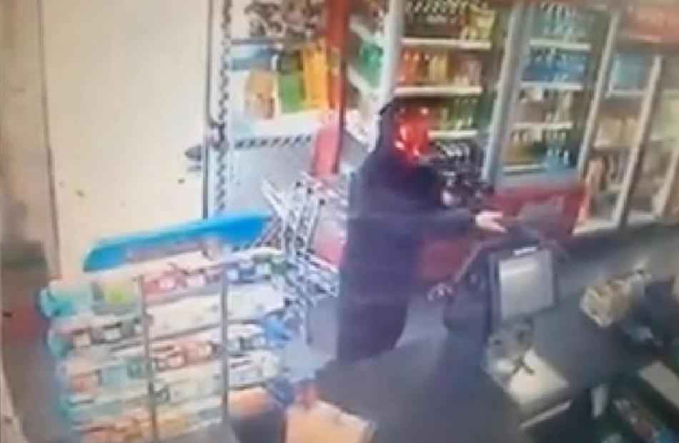 An armed offender wearing a devil mask points a rifle at a shop assistant during a robbery in...