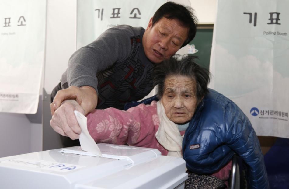 An elderly woman is assisted in casting her ballot in the presidential election at a polling...