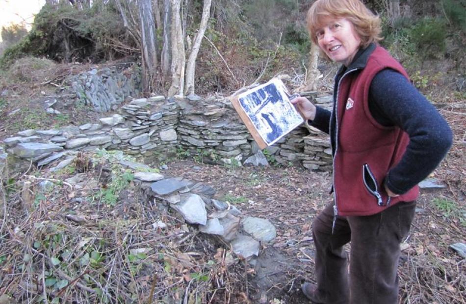 Archeological artist Jan Morrison, of Arrowtown, holds an archive picture of the stone...
