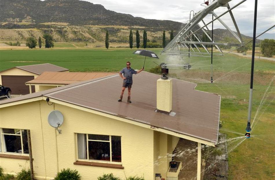 Bendigo Station stock manager Sam Macdonald, on his house roof, prepares for an irrigator to pass...