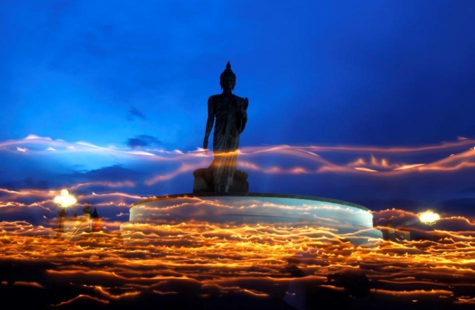 Buddhists carry candles while encircling a large Buddha statue during Vesak Day, an annual...