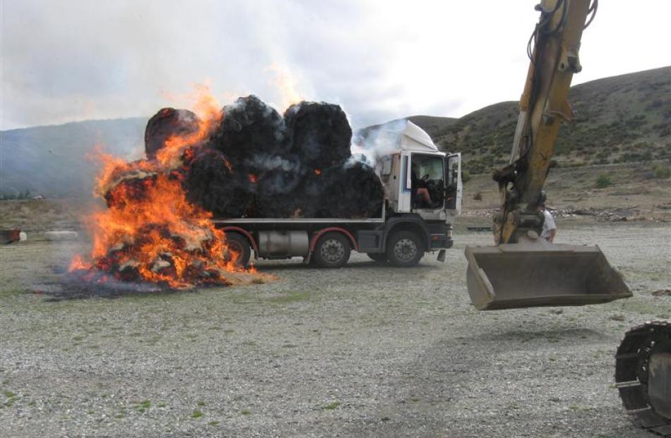 Burning bales pulled from the truck by a digger create an inferno as the digger driver prepares...
