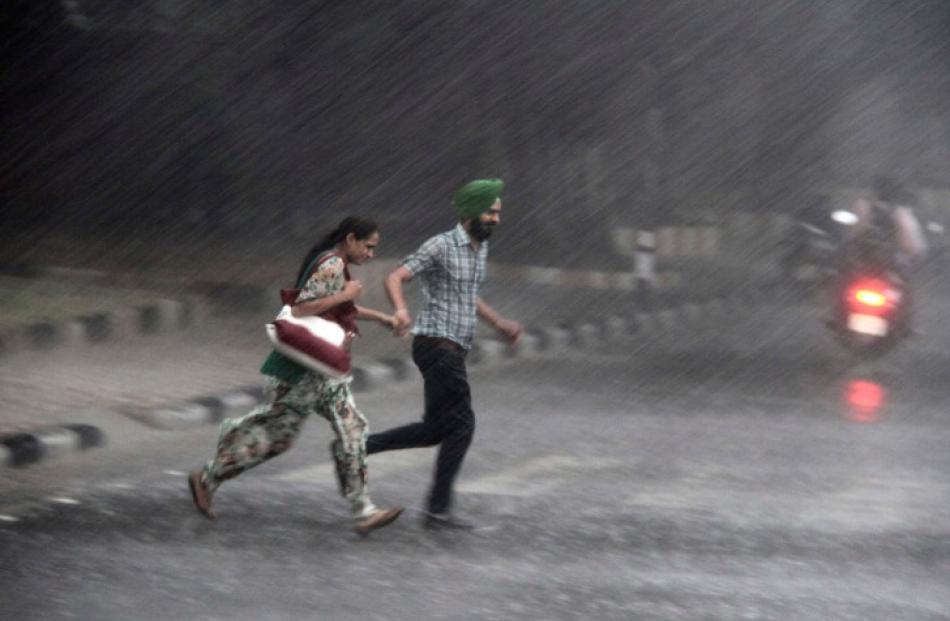 Commuters run for cover as they cross a road during monsoon rains in the northern Indian city of...
