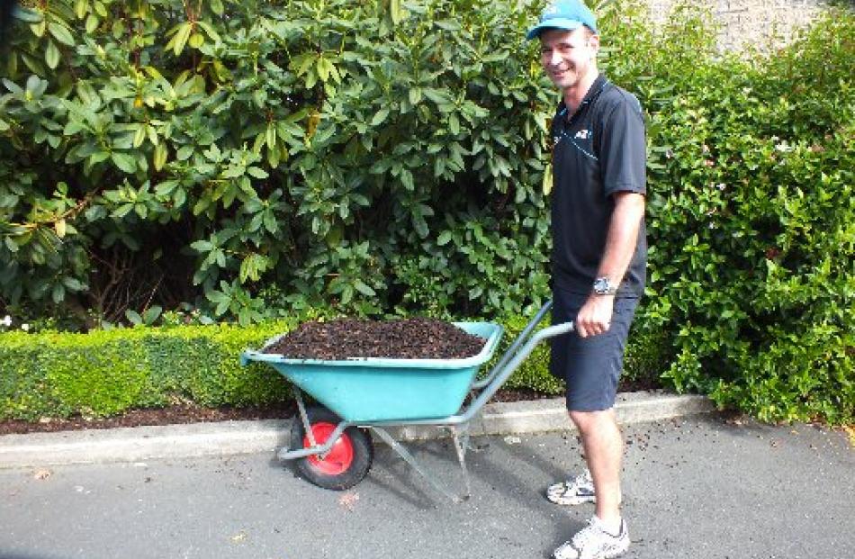 David Frame wheels a barrow load of woodchips during an ANZ working bee at the hospice.