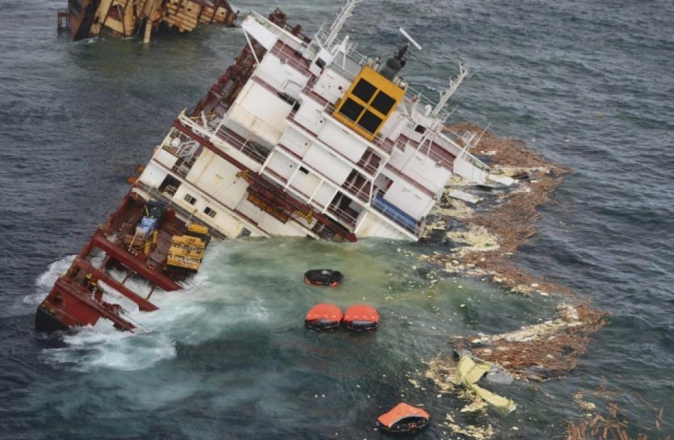 Debris floats around the remains of the stricken container ship Rena as it submerges, about 14...