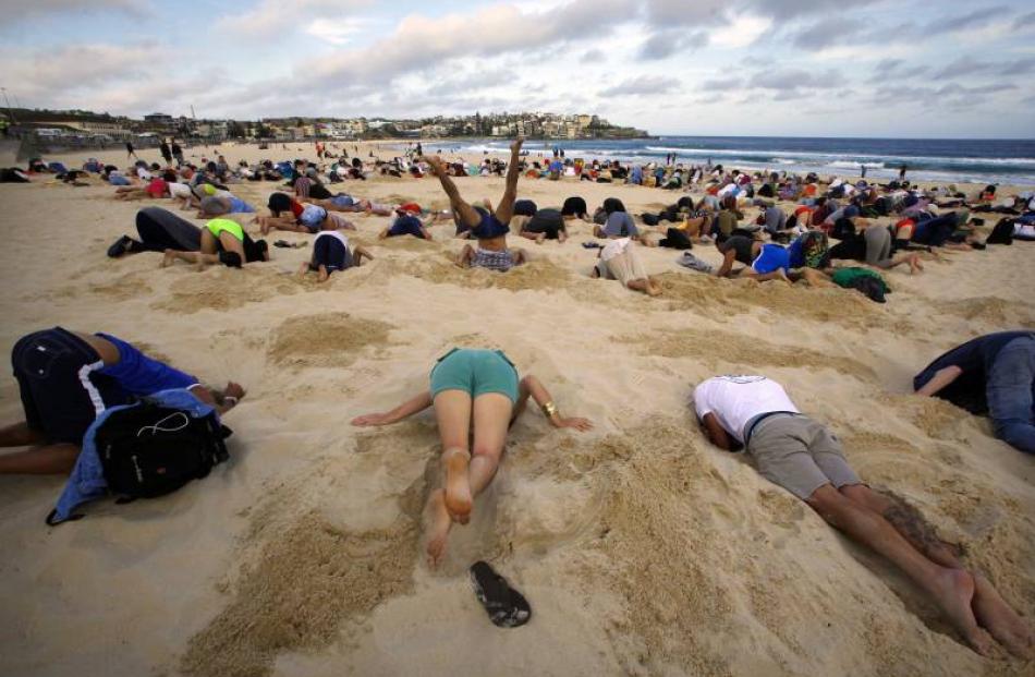 Demonstrators bury their heads in the sand at a Sydney beach before the G20 summit, in response...