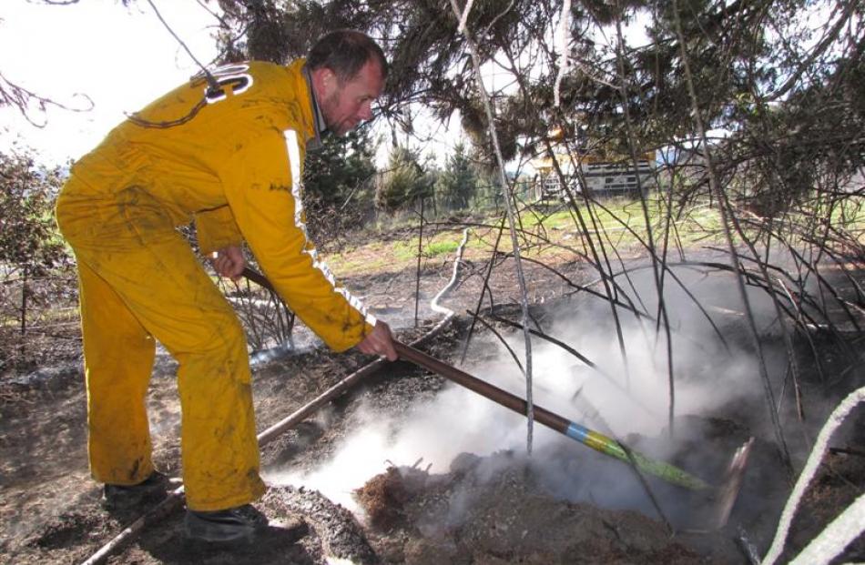 Department of Conservation rural firefighter Mark Mawhinney, of Queenstown, rakes over smoky...