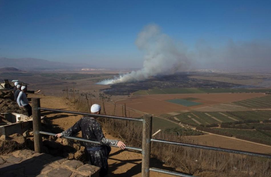 Druze men look at smoke rising on the Israeli-controlled side of the line dividing the Israeli...