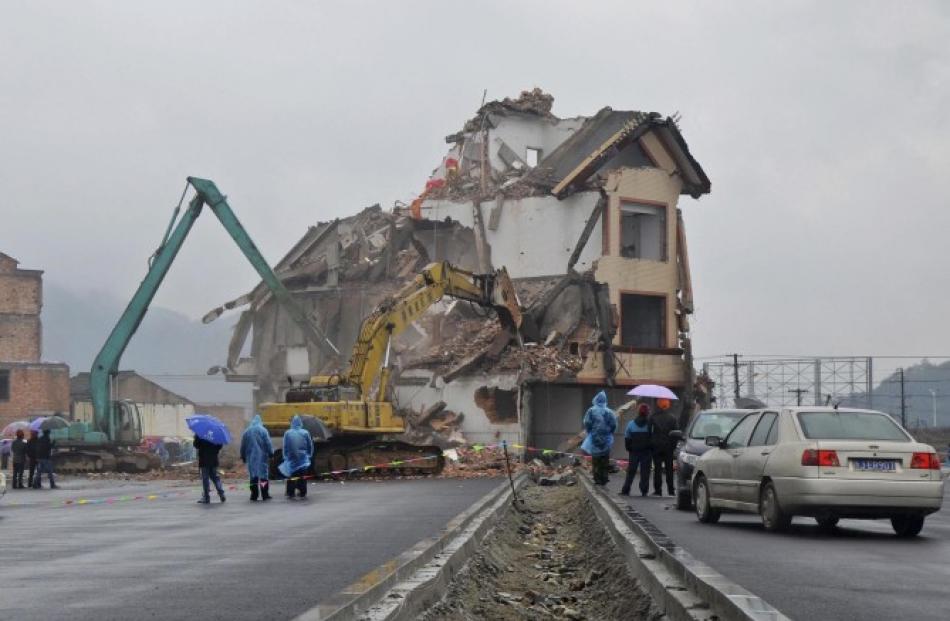 Excavators demolish the house of Luo Baogen in the middle of a newly built road in Wenling,...