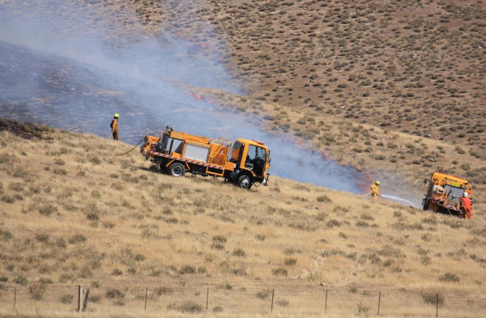 Firefighters spray water on one section of a  the grass fire near Tarras yesterday.Photos by...
