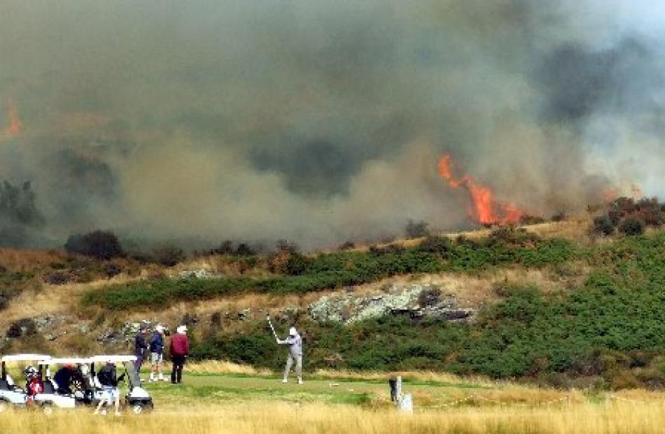 Golfers tee off while the fire rages in the background.